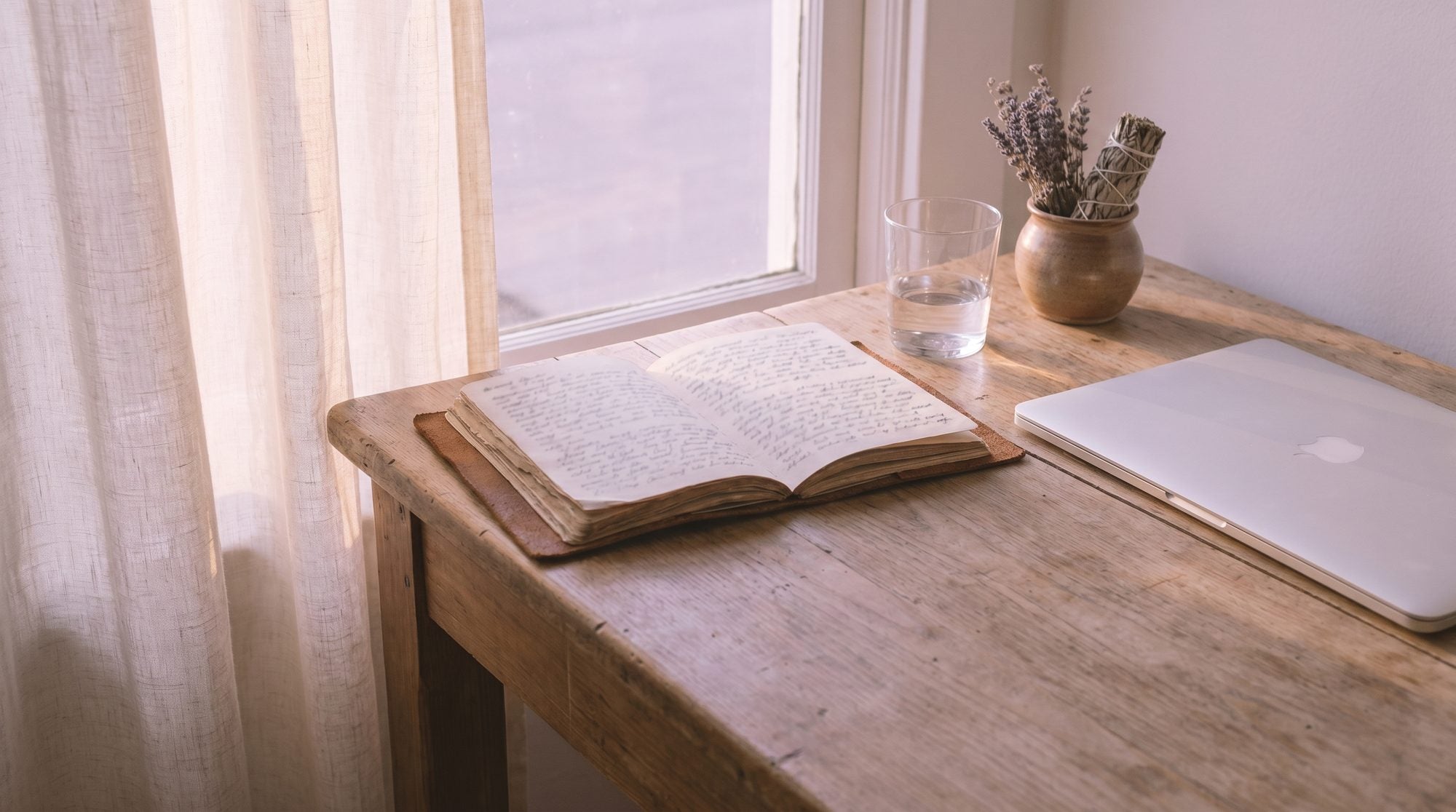 A calm sunlit workspace with journal, water glass, and lavender — no coffee mug visible